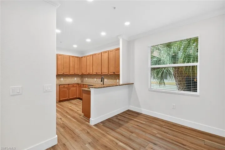 Kitchen with tasteful backsplash, light stone counters, light wood-style floors, recessed lighting, and crown molding