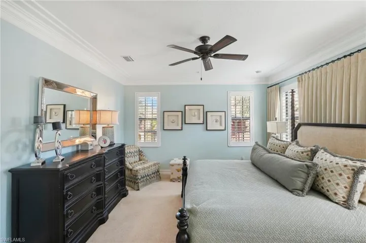 Bedroom featuring ceiling fan, light carpet, baseboards, visible vents, and ornamental molding