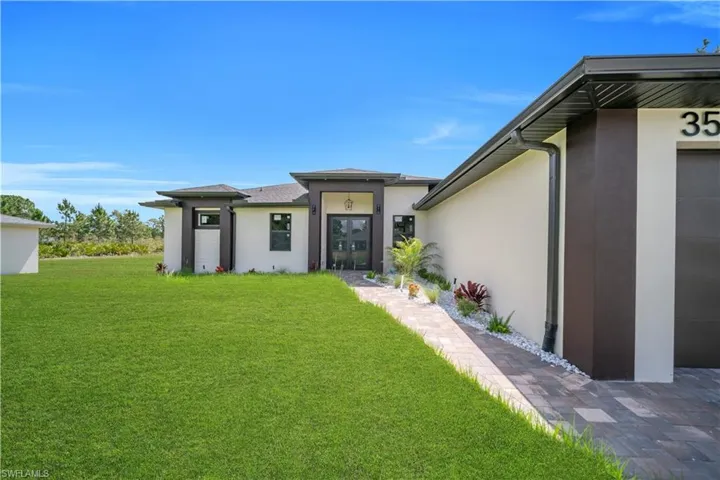 Modern exterior featuring a prominent entry, paver walkway, contemporary landscaping, well-maintained lawn, and a dark garage door