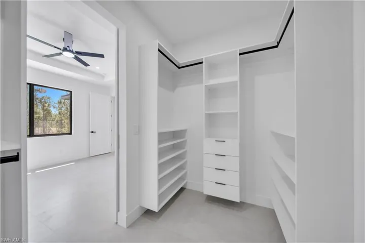 Walk-in closet with built-in white shelving, integrated drawers with black pulls, and hanging rods