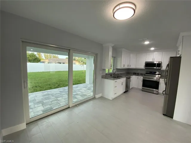Kitchen with dark stone counters, white cabinetry, appliances with stainless steel finishes, and sink