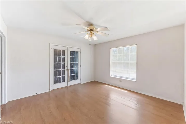 Virtually emptied den  with french doors, ceiling fan, and light wood-style floors