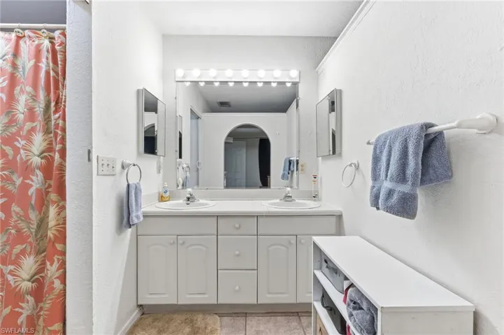 Full bathroom with double vanity, a textured wall, a shower with shower curtain, and light tile patterned floors