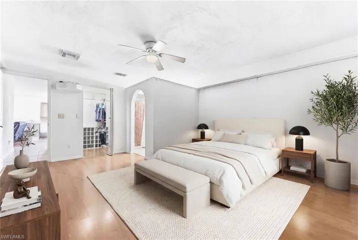 Virtually staged main bedroom with light wood-type flooring, arched walkways, a closet, and a ceiling fan