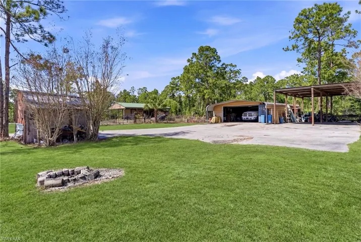 View of green lawn featuring a carport, a detached garage, and a fire pit