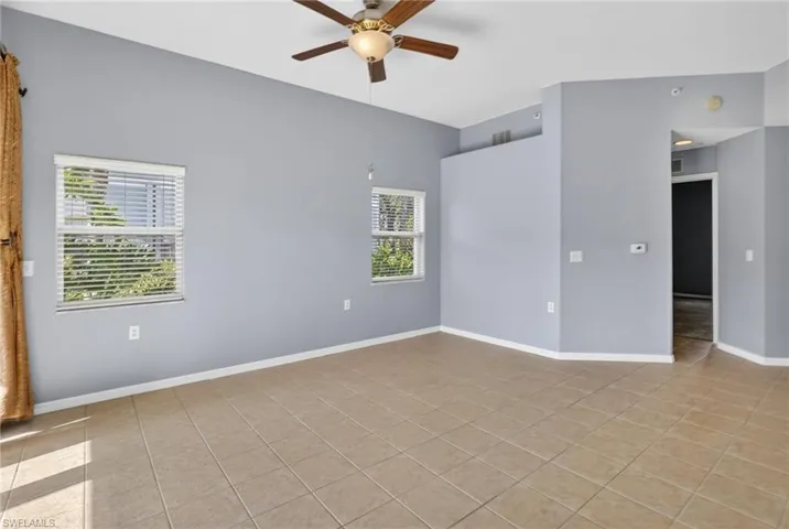 Vaulted ceiling with an attached ceiling fan, two windows with blinds, and tile flooring