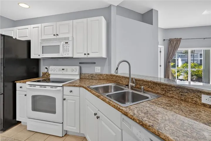 Kitchen featuring white cabinetry, granite countertops, tile flooring, a double basin stainless steel sink with a gooseneck faucet, and white appliances including an electric range and built-in microwave