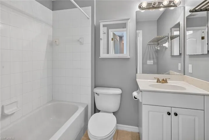 Bathroom featuring a white subway-tiled shower surround, a built-in bathtub, a white vanity with a light-toned countertop, a large wall-mounted mirror, and a wall-mounted medicine cabinet