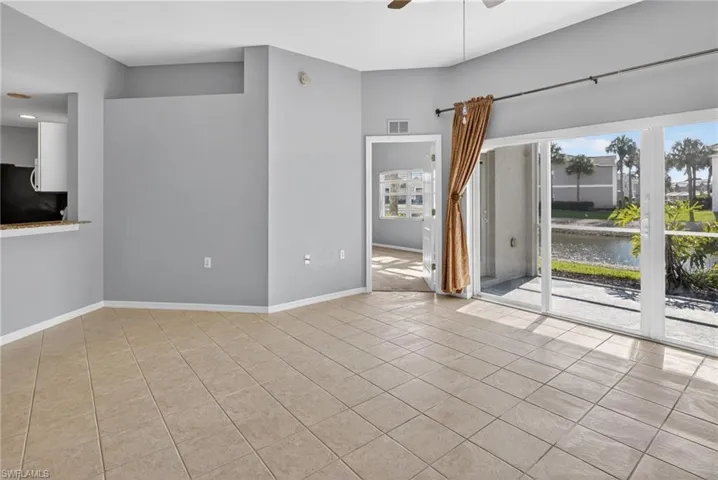 Living area featuring neutral tile flooring, a ceiling fan, and a pass-through window to the kitchen