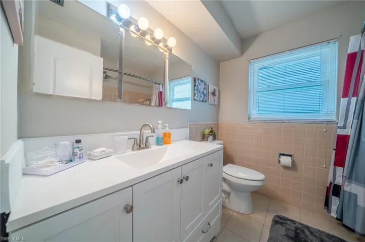 Bathroom featuring tile patterned flooring, vanity, tile walls, a shower with curtain, and a wainscoted wall