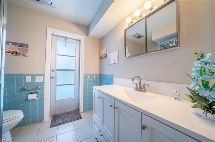 Bathroom with tile walls, healthy amount of natural light, a wainscoted wall, tile patterned flooring, and vanity