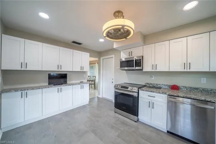 Kitchen featuring appliances with stainless steel finishes, white cabinets, light stone counters, and recessed lighting
