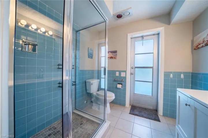 Full bathroom featuring tile walls, tile patterned flooring, vanity, a stall shower, and wainscoting