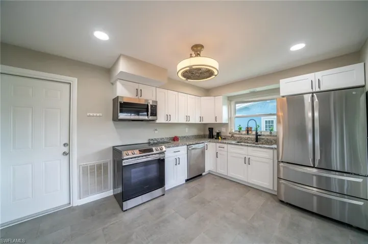 Kitchen with stainless steel appliances, light stone counters, white cabinetry, and recessed lighting