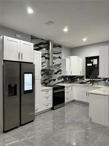 Kitchen featuring white cabinets, black / electric stove, a sink, stainless steel refrigerator with ice dispenser, and wall chimney range hood