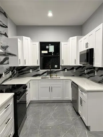 Kitchen featuring marble finish floor, stainless steel microwave, a sink, dishwashing machine, and electric range
