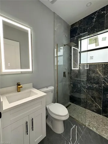 Bathroom with marble finish floor, a marble finish shower, toilet, and vanity