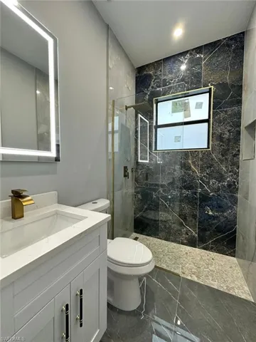 Bathroom with marble finish floor, toilet, vanity, and a marble finish shower
