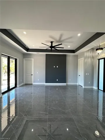 Empty room with a ceiling fan, a raised ceiling, and baseboards