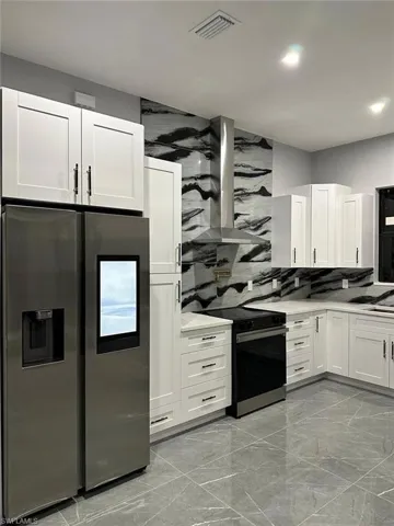 Kitchen with visible vents, marble finish floor, black range with electric cooktop, stainless steel refrigerator with ice dispenser, and ventilation hood