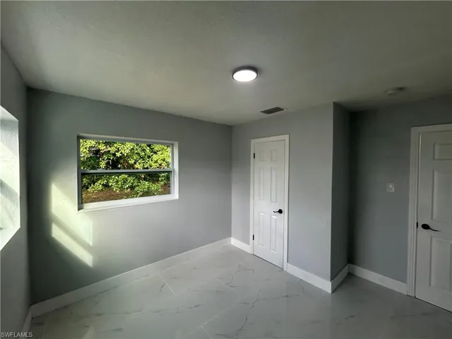 Empty room with a textured ceiling, marble finish floor, visible vents, and baseboards