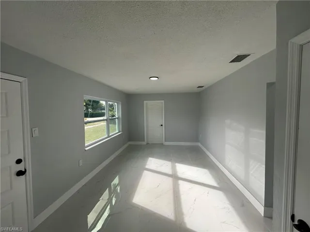 Spare room featuring marble finish floor, baseboards, visible vents, and a textured ceiling