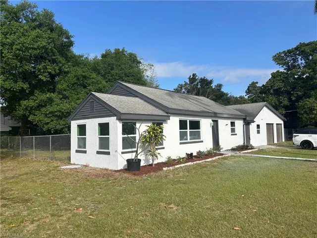 View of front of property with a garage, fence, roof with shingles, stucco siding, and a front yard