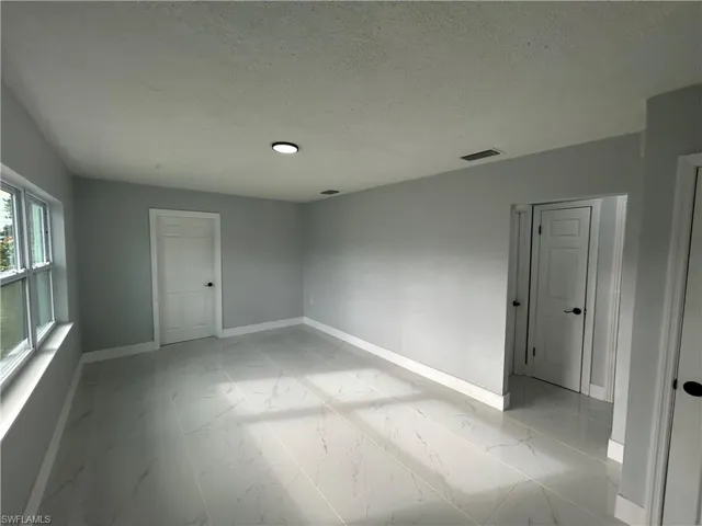 Empty room with marble finish floor, visible vents, a textured ceiling, and baseboards
