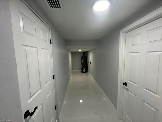 Hall featuring marble finish floor, water heater, visible vents, and baseboards