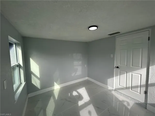 Unfurnished room with a textured ceiling, marble finish floor, visible vents, and baseboards