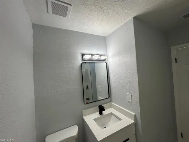 Half bathroom with a textured ceiling, a textured wall, toilet, vanity, and visible vents