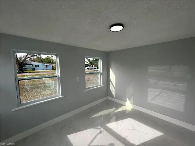 Empty room with marble finish floor, baseboards, and a textured ceiling