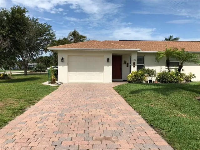 Single story home featuring a garage, stucco siding, a front lawn, and decorative driveway