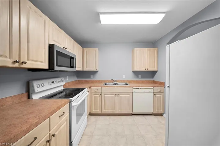 Kitchen featuring white appliances, light wood finish cabinets, light countertops, and light tile patterned floors