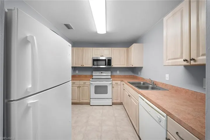 Kitchen featuring white appliances, light countertops, light wood finish cabinets, and light tile patterned floors