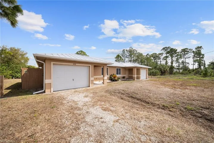 Single story home with stucco siding, a garage, dirt driveway, and a standing seam roof