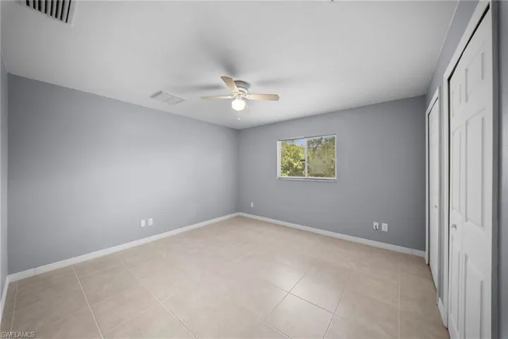 Unfurnished bedroom featuring a ceiling fan, two closets, and light tile patterned flooring