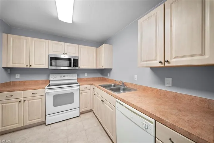 Kitchen with white appliances, light countertops, light wood finish cabinetry, and light tile patterned floors
