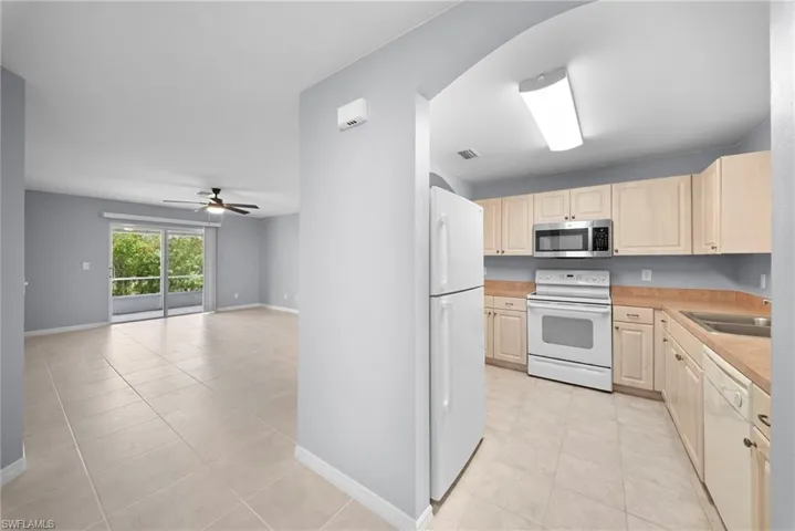 Kitchen featuring white appliances, light countertops, light wood finish cabinetry, and light tile patterned flooring