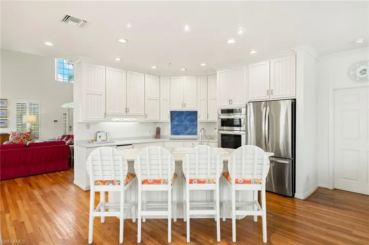 Kitchen with stainless steel appliances, light countertops, white cabinetry, an island with sink, and a breakfast bar area