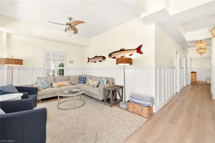 Living area featuring a chandelier, wood finished floors, a decorative wall, a ceiling fan, and wainscoting