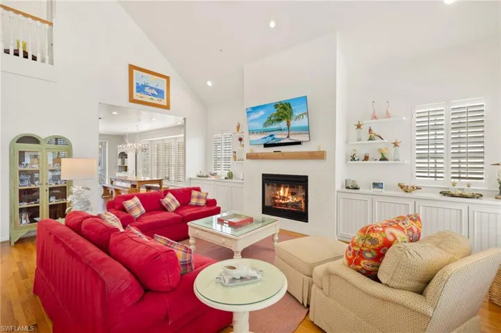 Living room featuring wood finished floors, healthy amount of natural light, a glass covered fireplace, recessed lighting, and high vaulted ceiling