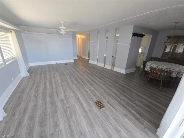 Unfurnished living room featuring wood finished floors, a ceiling fan, and baseboards