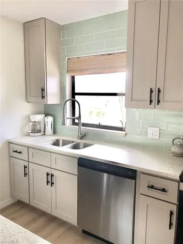 Kitchen with dishwasher, light stone counters, light wood-style flooring, and decorative backsplash