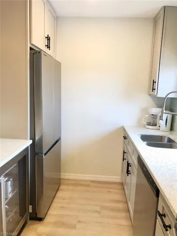 Kitchen featuring light stone countertops, stainless steel appliances, wine cooler, and light wood-type flooring
