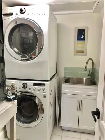 Laundry area with stacked washing machine and dryer, light tile patterned floors, and cabinet space