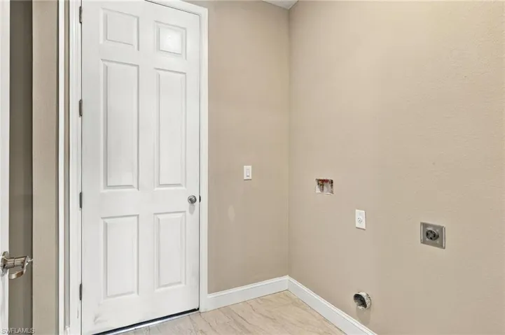 Six-panel interior door with brushed metal hardware and neutral-toned walls featuring designated utility hookups and electrical outlets over wood-finish flooring