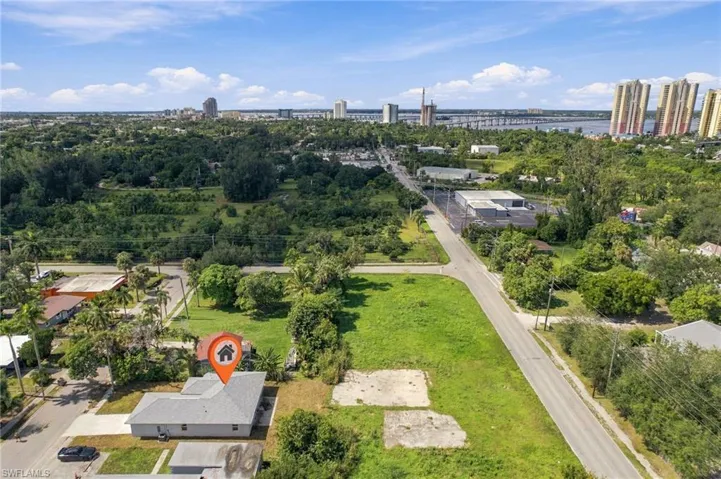 Aerial perspective of a single-story residence featuring a shingled roof, concrete driveway, and expansive parcel with established greenery