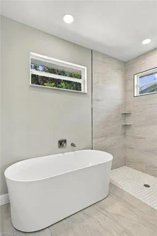 Freestanding soaking tub with wall-mounted plumbing, recessed ceiling lighting, walk-in shower with large-format wall tile and built-in shelving, and hexagonal floor tiling
