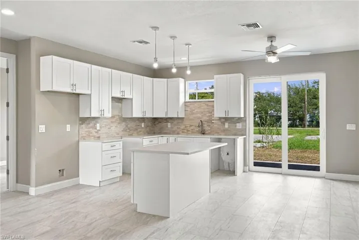 Kitchen featuring white shaker-style cabinetry, stone-finish backsplash, central island, three hanging pendant lights, and sliding glass doors